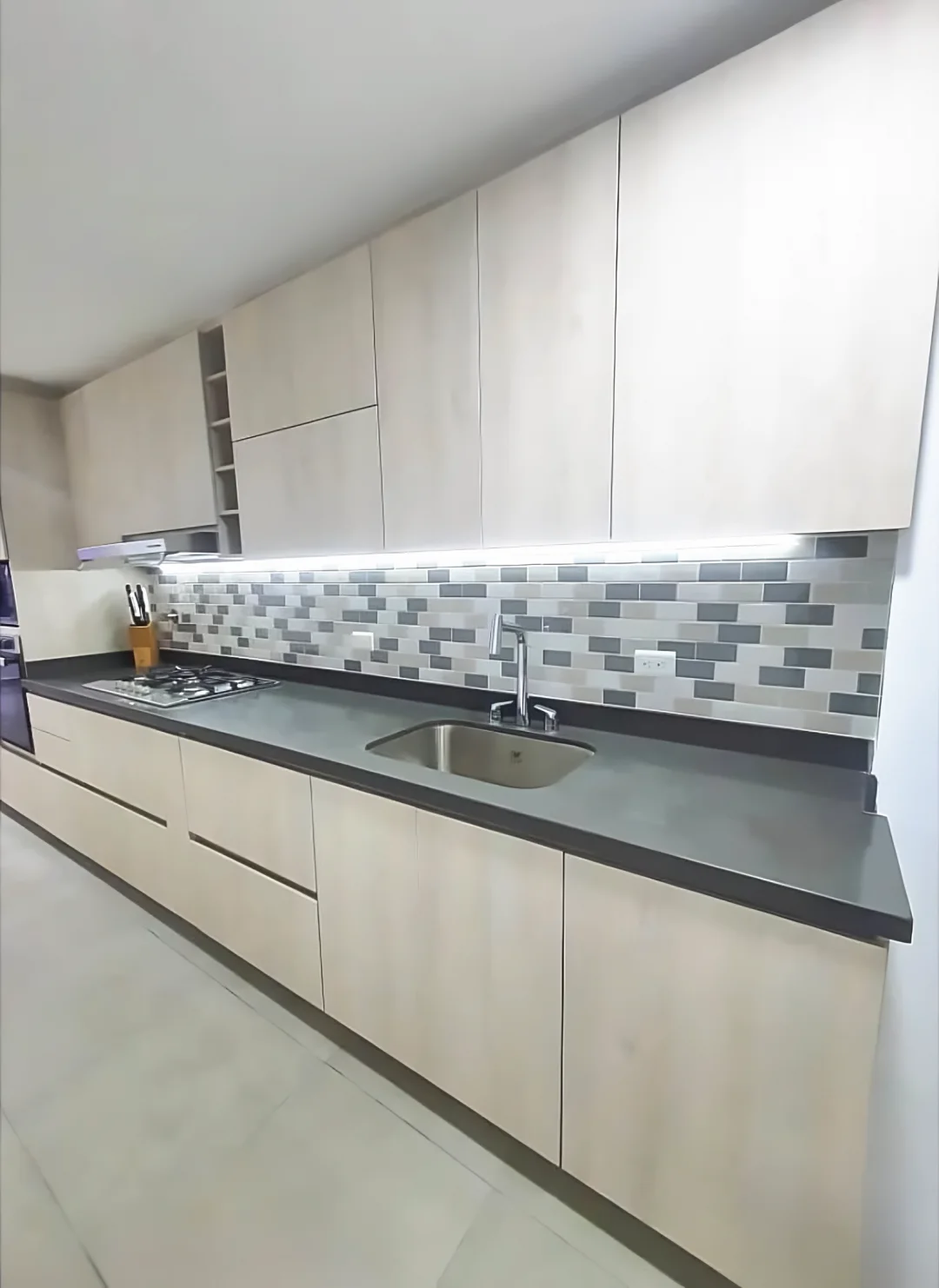 Cocina lineal terminada con muebles en tono roble gris, mesón oscuro, enchape en tableta y luz bajo las alacenas
