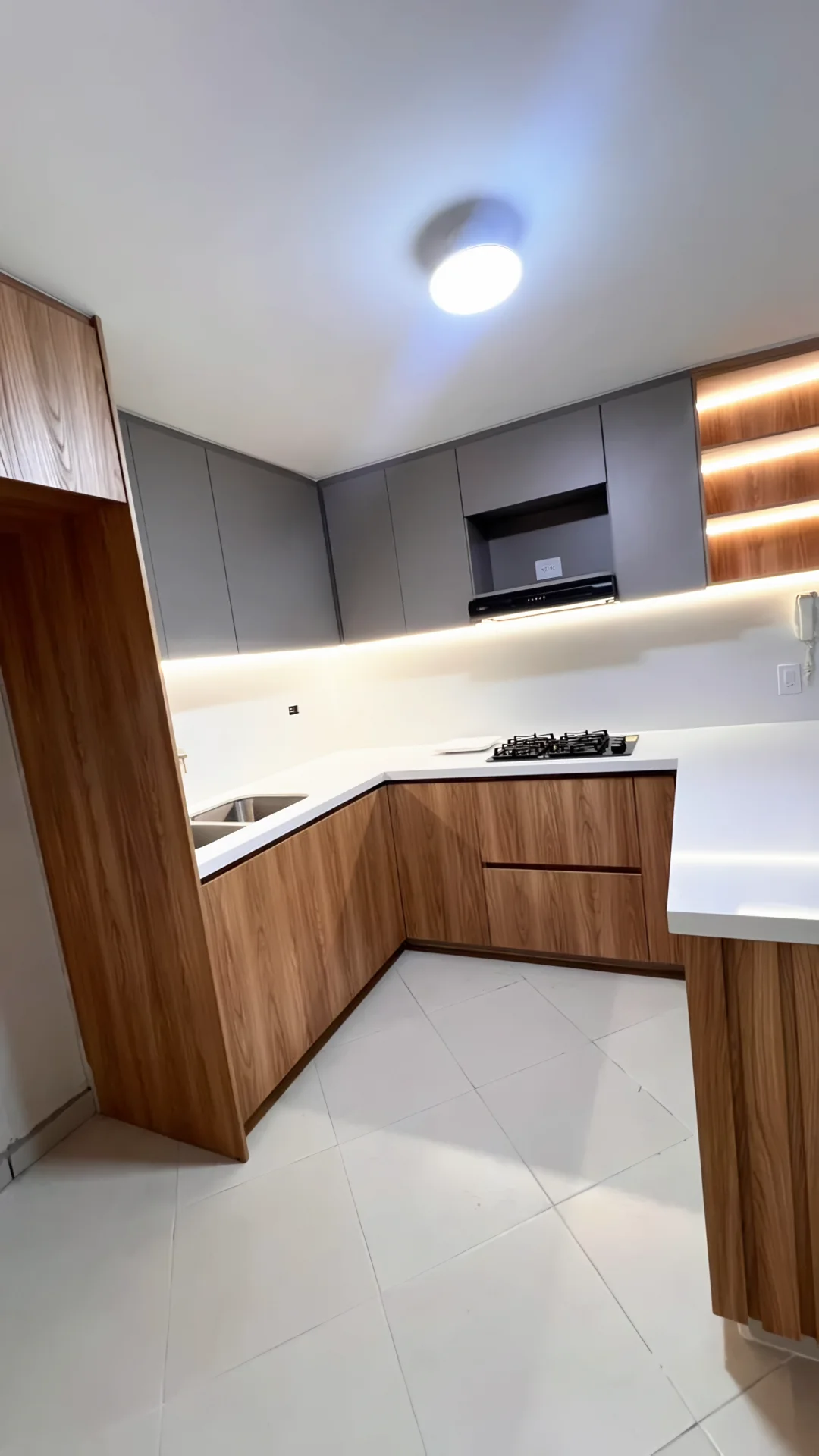 Esquina de la cocina en U con muebles bajos en madera, mesón blanco iluminado y repisas de luz cálida
